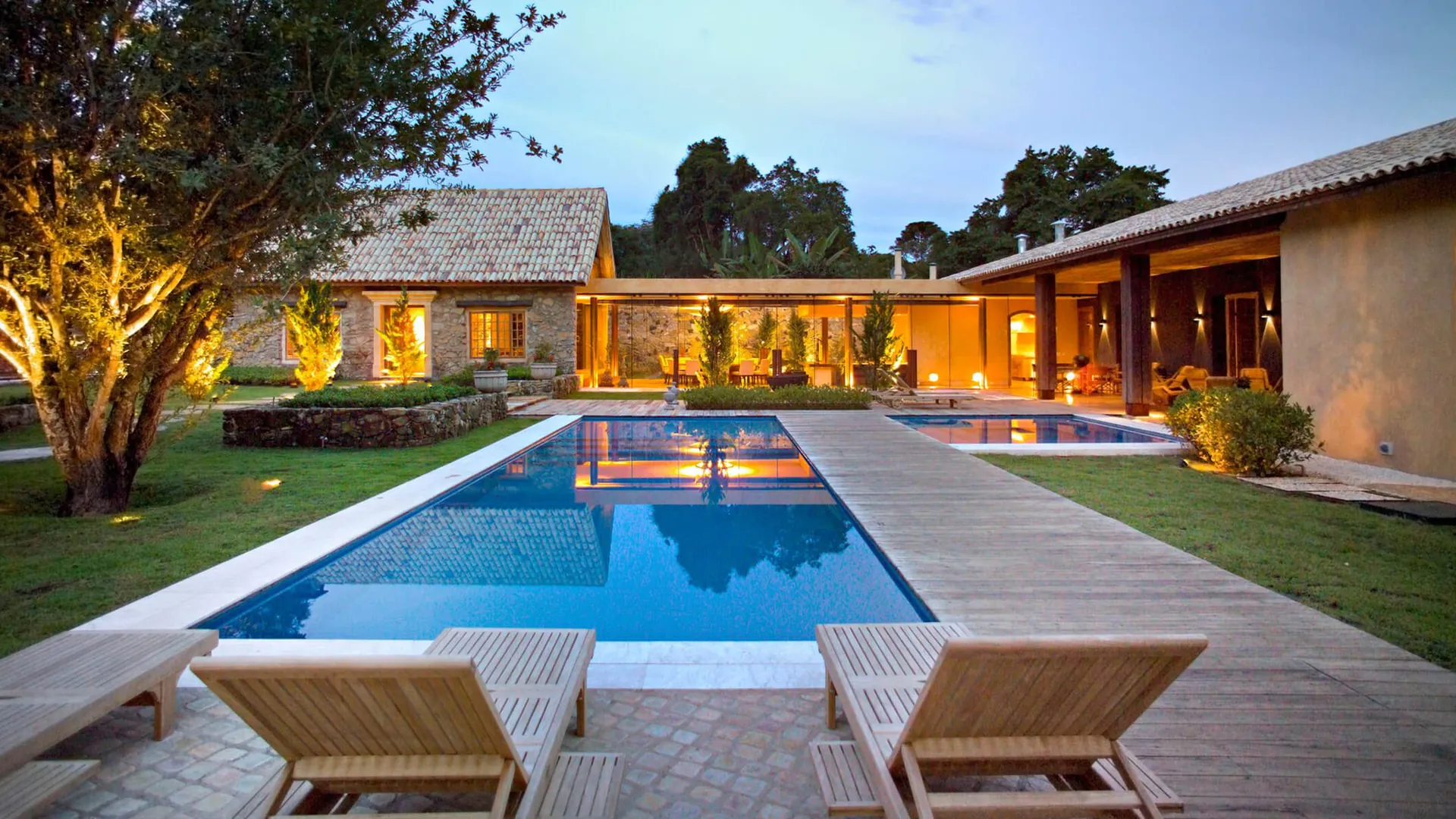 Casa do Sítio iluminada ao entardecer, com piscina